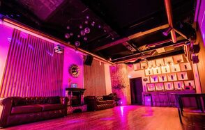 LoftForParty. Бэкстейдж лофт . Тёмное помещение с низким потолком, кожаные диваны, барная стойка, разноцветное освещение, стены отделаны деревянными панелями и кирпичом, металлические трубы на потолке, зеркальный декор, дискоболы, деревянный пол.