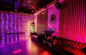 LoftForParty. Бэкстейдж лофт . Кирпичная стена с фиолетовой подсветкой, пластиковые стулья, диваны из тёмной кожи, деревянный пол, подвесной светильник, зеркало с подсветкой, декоративное зеркало на стене, мебель и стены в теплых тёмных тонах.