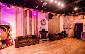 LoftForParty. Бэкстейдж лофт . Простор с деревянным полом и светлыми стенами, декорированными вертикальными панелями. Две коричневые кожаные софы, зеркало, настенное декоративное зеркало, несколько подвесных диско-шаров, сцена с DJ-аппаратурой, разноцветное освещение.