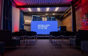 MPSellers(МПСеллерс). Просторный зал для мероприятий. Пространство в стиле лофт с кирпичными стенами и металлическим потолком, с проектором и экраном. Ряд черных кресел, синий занавес, разноцветная подсветка. Надпись на экране: "MPSELLERS BUSINESS CLUB".