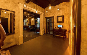 Tangiers Lounge(Танжер Лаундж) . Стильное пространство с антикварными элементами: арочная ниша, зеркала в резных рамах, плиточный пол, приглушённое тёплое освещение с подвесными лампами, деревянный стол с монитором. Стены с фактурной отделкой, некоторые декорированы пустыми рамками.