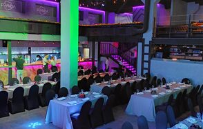 PRAVDA(Правда). Просторный зал на 800 гостей. Большое помещение с несколькими уровнями, длинные банкетные столы с белыми скатертями и черными стульями, яркое цветное освещение, лестница, барная стойка с подсветкой. Стены и потолок темные, оформлены неоновой подсветкой. Текст: "PANDA".