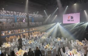 СВОБОДА. Зал на 1200 человек. Большое праздничное пространство с верхним уровнем, декорированное струнными светильниками. Расставлены круглые столы с белыми скатертями, окруженные белыми стульями. На стене экран с логотипом. Общий свет направлен на столы.