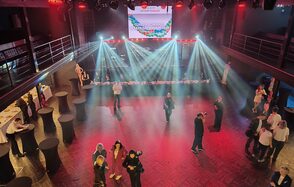 СВОБОДА. Зал на 1200 человек. Многоуровневое пространство с деревянным полом, окруженное перилами. В центре люди, по периметру высокие столы с черными скатертями. На сцене сзади стоит экран, над которым проецируется свет. Освещение яркое, цветное.