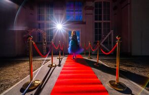 Лофт КОСМОС с летней верандой. Красная ковровая дорожка окружена бархатными канатами на золотых стойках. Пространство перед зданием с высокими окнами. Яркий свет направлен на дорожку. Декоративная арка справа. Северное сияние в небе.