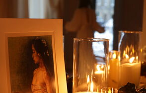 Лофт Поле. Уютный зал для мероприятий. Крупный план свечей в прозрачных стеклянных подсвечниках. На переднем плане изображение с портретом женщины. Вдалеке размытый силуэт человека у окна. Интерьер в тёплых тонах.