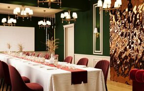 Вегас. Атмосферный лофт с акцентным дизайном. Пространство для мероприятий с длинным накрытым столом, окружённым бордовыми стульями. Зеленые стены с белыми панелями и декоративной панелью из металла. Золотые люстры и бра с белыми абажурами, деревянный пол, декор в виде сухих трав.