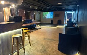 BULL LOFT(Лофт Бык) . Лофт-пространство с деревянными полами, барной стойкой, барными стульями, диванами, кирпичными стенами и экраном на стене. Современное освещение, тёмные потолки и декоративные панели.