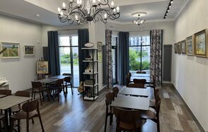 Арт Холл. Просторное помещение с паркетным полом и белыми стенами, украшенными картинами. Зал обставлен деревянными столами и стульями, освещен двумя люстрами. Вдоль одной стены расположены окна с синими шторами, межкомнатные перегородки отсутствуют.