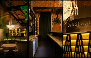 Arsenal Loft(Арсенал Лофт). Лофт-пространство с кирпичными стенами и арочными потолками. Зона барной стойки с деревянными столешницами, полки с декоративными бутылками. Круглый стол и стулья. Крупная хрустальная люстра. Надпись "LOFT & CATERING". Теплое освещение.