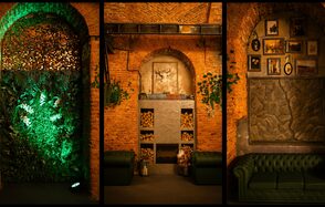 Arsenal Loft(Арсенал Лофт). Арочное пространство из кирпича с элементами декора; слева стена с зеленью и подсветкой; в центре полки с дровами и изображение оленя; справа зеленый диван, настенная картина и декор из картин. Освещение теплое, интерьер в темных и зеленых тонах.