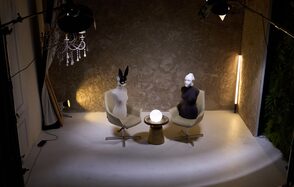 WhiteFox Studio(Студия Белая Лиса). Помещение с двумя креслами и круглым столиком между ними, на котором светится шар. На креслах находятся манекены. На стене серая текстурная поверхность, светодиодная лампа стоит вертикально справа. Светлый пол и подвесная люстра.