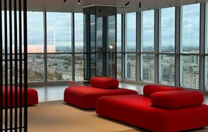 Арт-Плейс Фактура. Современный лофт с видом на весь город. Современное помещение с окнами от пола до потолка, открывающими вид на город. В интерьере красные мягкие диваны и бежевый пол. Потолочные светильники обеспечивают искусственное освещение. Декор из стекла и металла.