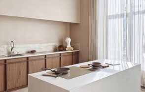 Киото. Светлый зал с кухней. Кухонное пространство с белым островом в центре, деревянными шкафами, мраморной столешницей и раковиной. Светлые шторы от пола до потолка. На столе посуда и кухонные принадлежности. Светлые нейтральные стены.