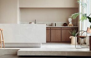 Киото. Светлый зал с кухней. Современное пространство с кухонной зоной. Белая мраморная барная стойка, светло-коричневые деревянные шкафы, металлический стул с кожаным сиденьем. Горшечные растения и бюст на колонне. Светлые тона, обилие естественного света.