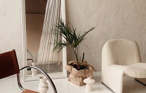 Киото. Светлый зал с кухней. Современное пространство с белыми стенами и текстурированной отделкой. Светлое кресло, коричневый стул с металлическими подлокотниками, большое зеркало, комнатное растение в бумажной упаковке. Белые декоративные предметы, светлый пол.