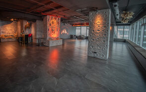 ATMOSFERA 53 (Атмосфера 53). Просторное помещение с бетонными колоннами и стенами, отделанными декоративной штукатуркой. Пол выложен темным кафелем, множество больших окон с видом на город. Имеется зона с креслами, декоративный камин. Освещение теплое, с акцентом на колонны.