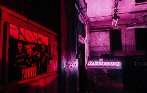 PVZ CLUB(ПВЗ Клуб). Небольшое пространство с неоновым розовым освещением, надписью на стене, индустриальными элементами, зеркальными поверхностями и граффити. Видны металлические конструкции, обветшалые стены, потолочные светильники и постер на стене.