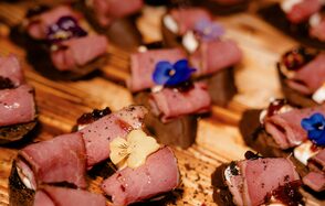 Атлас. Мультиформатная площадка. Маленькие закуски из рулетов мяса на деревянной поверхности, украшенные съедобными цветами.