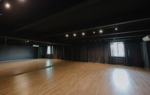 Танцевальный зал 70м2 студии RedHeartDance. Зал №2.. Просторное помещение с зеркальной стеной и деревянным полом. На потолке установлено точечное освещение. Стены и потолок темно-серые. По одной стене висят темные шторы, впереди виднеется окно. Помещение в отличном состоянии.
