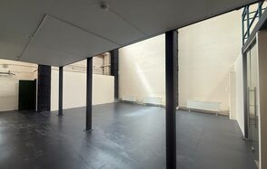 Просторный светлый лофт для мероприятий . Большое открытое пространство с высокими потолками и колоннами, серый пол, светлые стены. По бокам установлены радиаторы отопления. Естественное освещение падает через высокие окна.