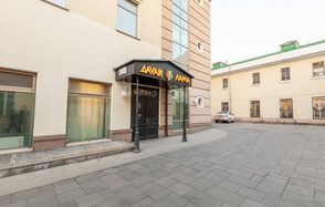 Давай Лама. Вход в здание с аркой, стеклянные окна, двери, вывеска с надписью на незнакомом алфавите.  Мощеная площадка перед входом в светлых тонах, подъездная дорожка. Фасад кремового и коричневого цветов с большим окном.