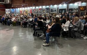 Выставочный зал Форум. Аудиторное пространство с креслами, сидят зрители. Стены из кирпича, на стенах выставка картин в подсвеченных витринах. Пол бетонный, хорошее яркое освещение.