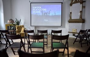 Артиста Лекторий. Комната для мероприятий с экраном, на котором проецируется текст. Стулья расставлены в ряды. В углу зелёные растения и жёлтое кресло. Светлая стена с белой плиткой и декоративной рамой. Лампа с абажуром на столике.