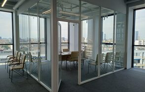 Аренда учебных аудиторий площадью 200 м². Переговорная комната с панорамными стеклянными стенами, оборудованная прямоугольным деревянным столом и кремовыми стульями. Естественное освещение через большие окна. Серый ковролин на полу. Белый потолок с трековыми светильниками.
