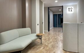 Лекторий на 53 этаже Москва-Сити - 100 м², до 35 человек. Современное помещение с бежевыми стенами и деревянным полом, светло-серый диван, журнальный столик. В центре - белая стойка. Наверху яркое освещение, на стене черный текст "BOVA". Слева деревянные панели.