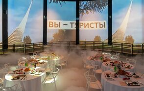 Атракцион до 80 человек. Круглое помещение с экранами, на которых изображены белые шпили и деревья на фоне синего неба. На экранах текст «ВЫ – ТУРИСТЫ». В центре стоят круглые столы с белыми скатертями, накрытые посудой и едой. Белые стулья, искусственный туман на полу.