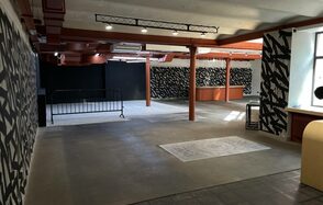 Бертгольд центр. Просторный лофт. Просторное помещение с бетонным полом, белыми и черными стенами с графическим рисунком. Красные металлические колонны и конструкции на потолке. Окно с естественным освещением, светильники на потолке. Металлическая баррикада, деревянная стойка.