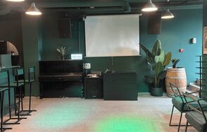 Work Shop Loft(Воркшоп Лофт). Зал 11 . Пространство с темно-зелеными стенами, проектором и экраном, задними колонками. Черное пианино, барные стулья и столы, декор в виде растений в горшках и деревянной бочки. Кафельный пол, подвесные светильники.