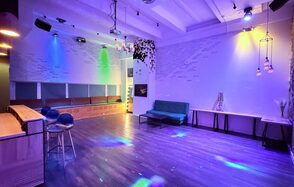 Barshowplace (БарШоуПлейс). Лофт для вечеринок с коктейльным баром . Пространство для мероприятий с деревянным полом, барной стойкой и высокими стульями. Стены декорированы цветным подсветкой, на потолке подвесные лампы. Имеются диваны, столики, велюровая обивка мебели. Настенные элементы из белого кирпича и древесины.