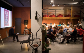 Стильный двухуровневый лофт. Человек ведёт лекцию. Слушатели смотрят на экран и лектора