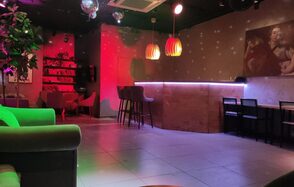 Work Shop Loft(Воркшоп Лофт). Зал 9. Лофт-пространство с барной стойкой, высокими стульями и диванами. На стене картина, рядом книжная полка. Цветное освещение с красными и зелёными акцентами. Потолочные светильники и зеркальный шар. Тёмный потолок, светлый пол, декоративные растения.