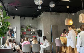 Work Shop Loft(Воркшоп Лофт). Зал 9. Лофт-пространство с серыми стенами и потолком, зона отдыха с мягкими стульями и столиками, барная стойка с высокими стульями, украшено растениями и полками с книгами, висят зеркальные шары и светильники, на стене картина, светильники на потолке.