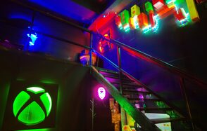 Лофт Геймеры. Лестница на второй этаж, под ней неоновая подвеска с игровым логотипом и неоновая лампа. 