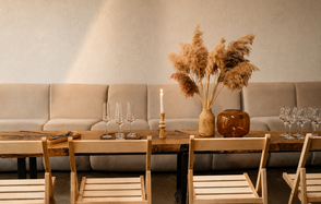 Light loft with light music and a bar. Пространство с деревянным столом и стульями, вдоль стены стоит мягкий диван. На столе декор в виде вазы с сухими травами, свеча и бокалы. Стены светлые, освещение мягкое. Цвета бежевый, коричневый и нейтральные тона.