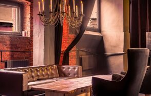 Music loft (Мьюзик лофт). Лофт-пространство с кирпичными стенами, деревянным столом и кожаными диванами. Над столом висит металлическая люстра с имитацией свечей. Кресло с высокой спинкой стоит рядом. Окно со шторами пропускает мягкий свет.